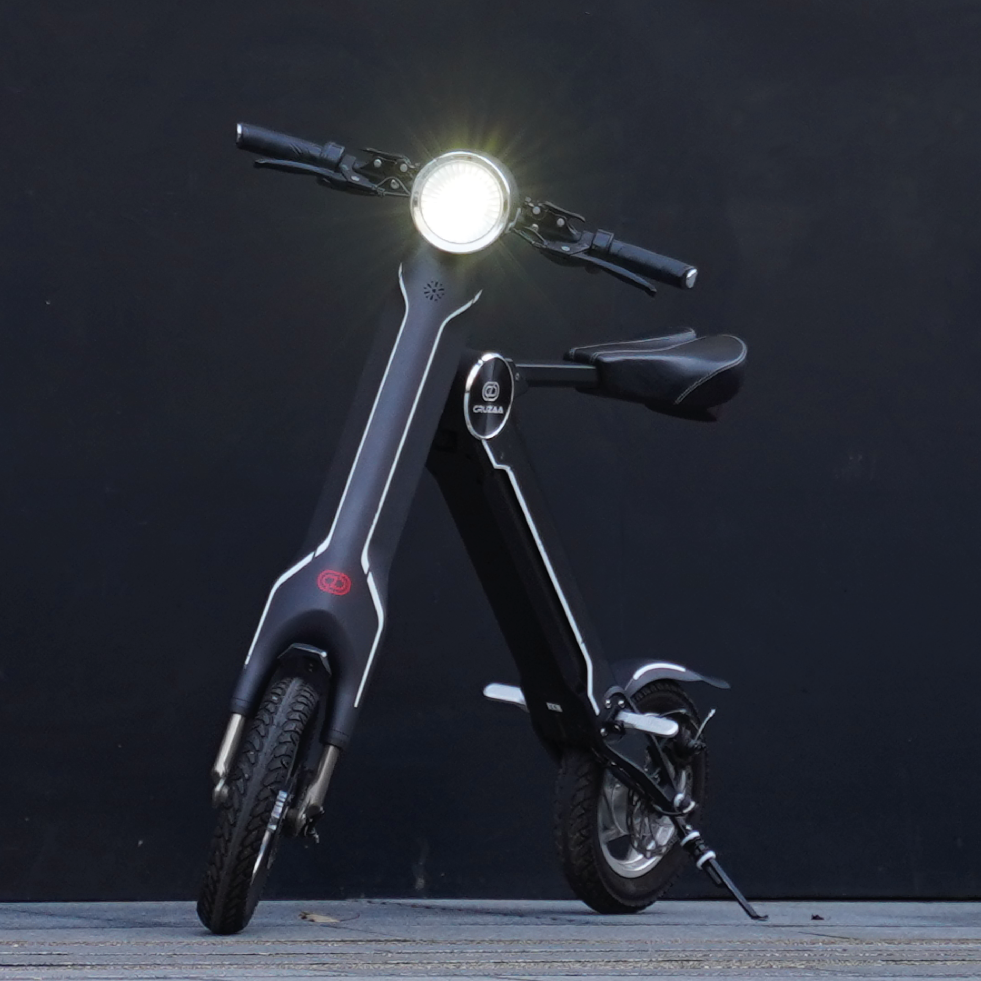 The Cruzaa E-Scooter in Carbon Black - Standing with headlight on in an urban setting.