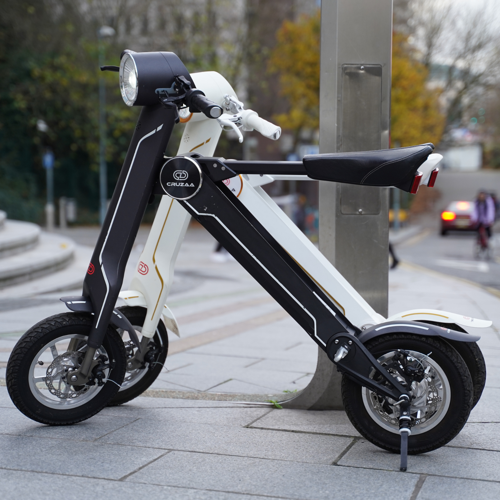 The Cruzaa E-Scooter Pro - Scooters in Carbon Black and Racing White colourways standing in an urban setting. 