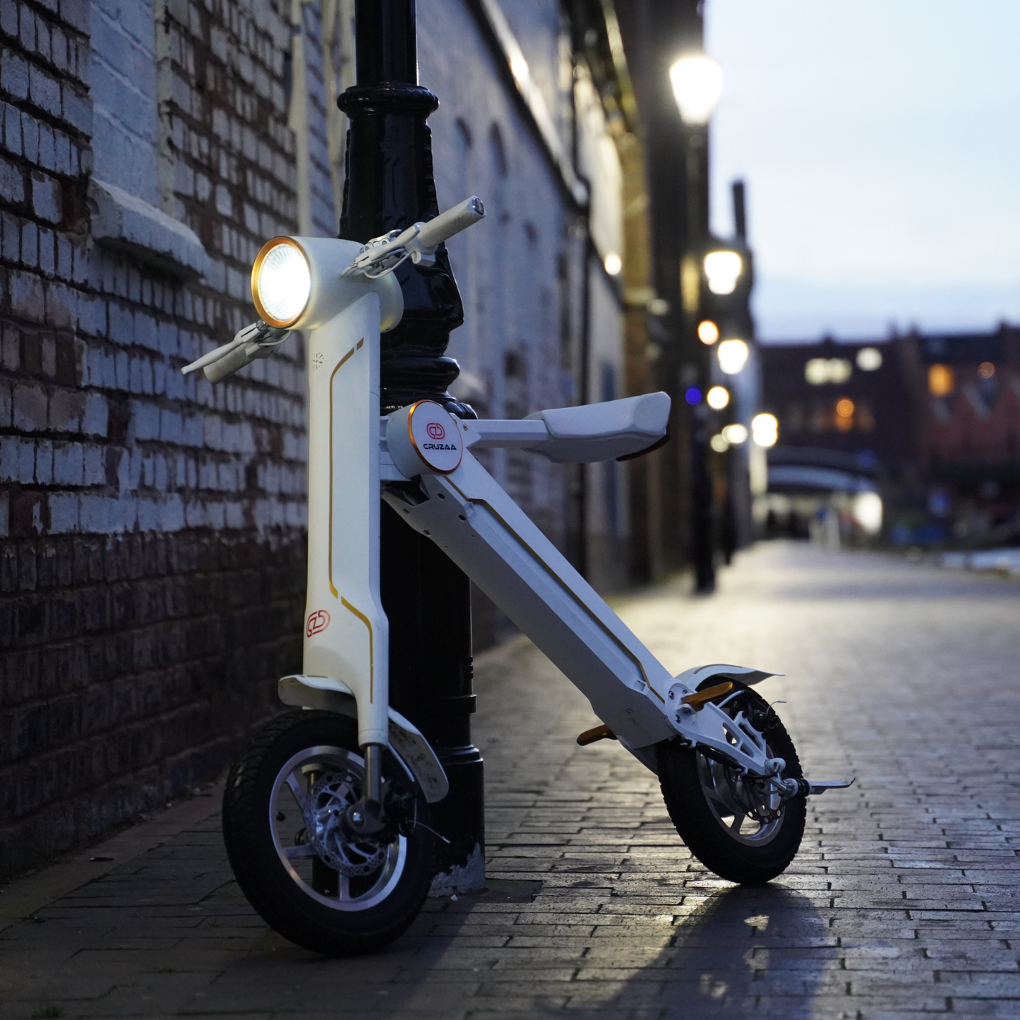 The Cruzaa E-Scooter in Racing White - Standing with headlight on in an urban setting.